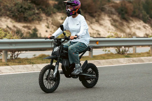 Person in full riding gear and helmet cruising down a paved road on a sleek black mini motorbike.