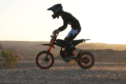 Person riding GT54 electric mini motorbike for kids and adults on rocky terrain at sunset