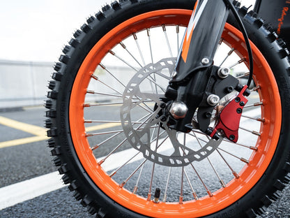 Close-up of GT54 electric mini motorbike front wheel with orange rim and disc brake on asphalt road