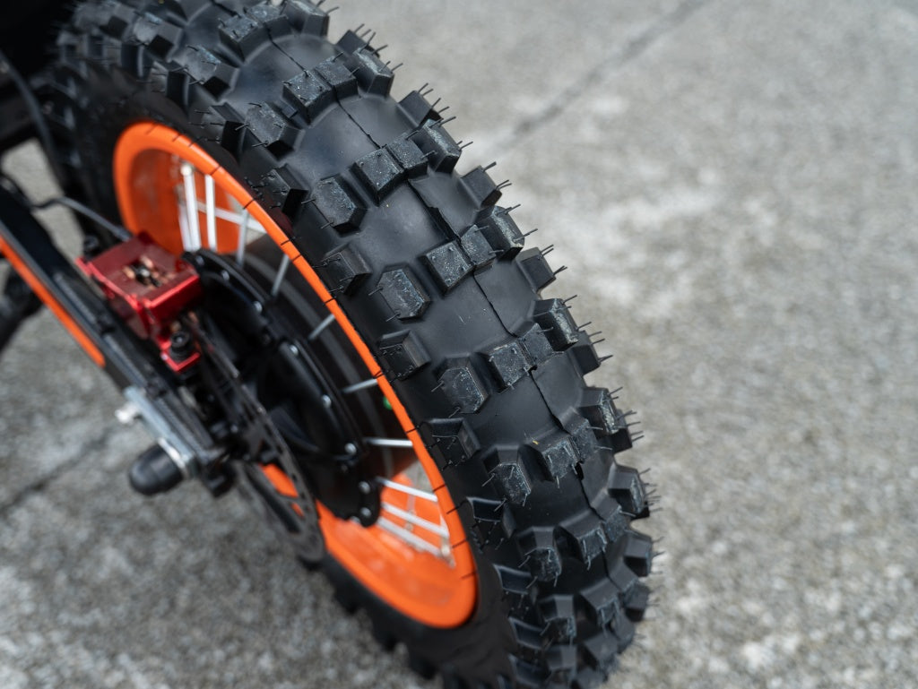 Close-up of GT54 electric mini motorbike's rugged off-road tire and orange wheel rim
