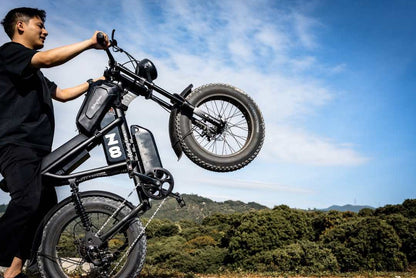 Black matte E-Bike with thick 20-inch all-terrain tires, sturdy frame, and front suspension being lifted by a person