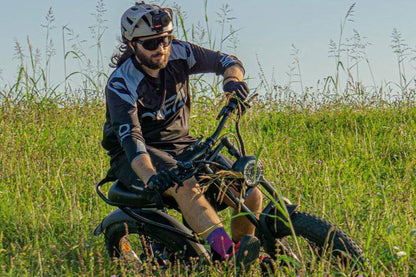 Off-road black E-Bike with fat tires ridden by a man wearing black and blue sportswear, helmet, and sunglasses