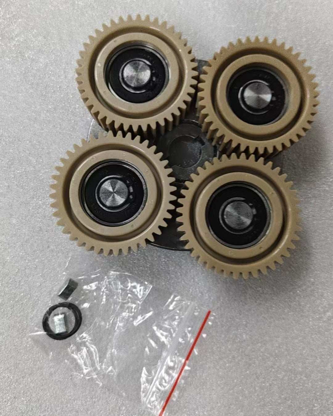 Motor Clutch Assembly with four beige gears and black centers on a grey surface, including small hardware pieces in plastic bags